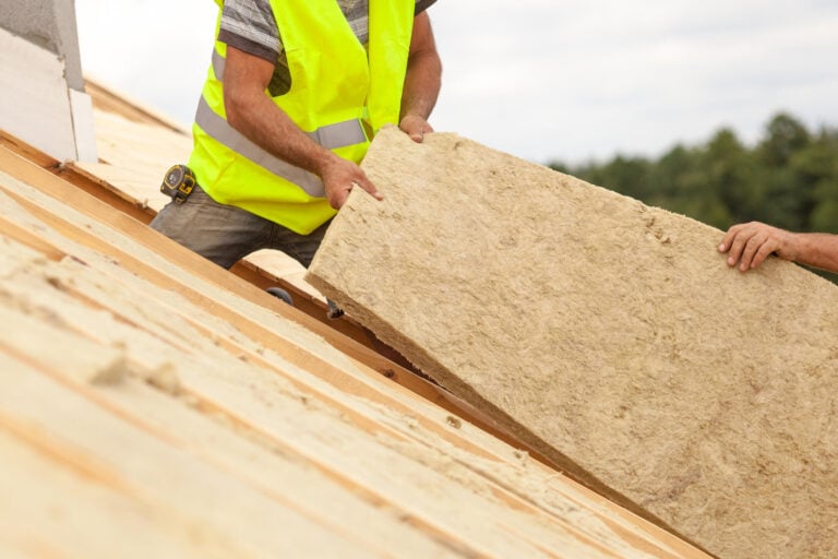 roof insulation-roofers installing panels of insulation into roof from on top of the trusses