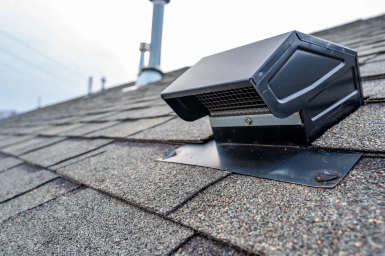 Close-up view of a rooftop vent expertly installed on a shingled roof, with a clear sky in the background. The rectangular, metallic design ensures efficient ventilation.