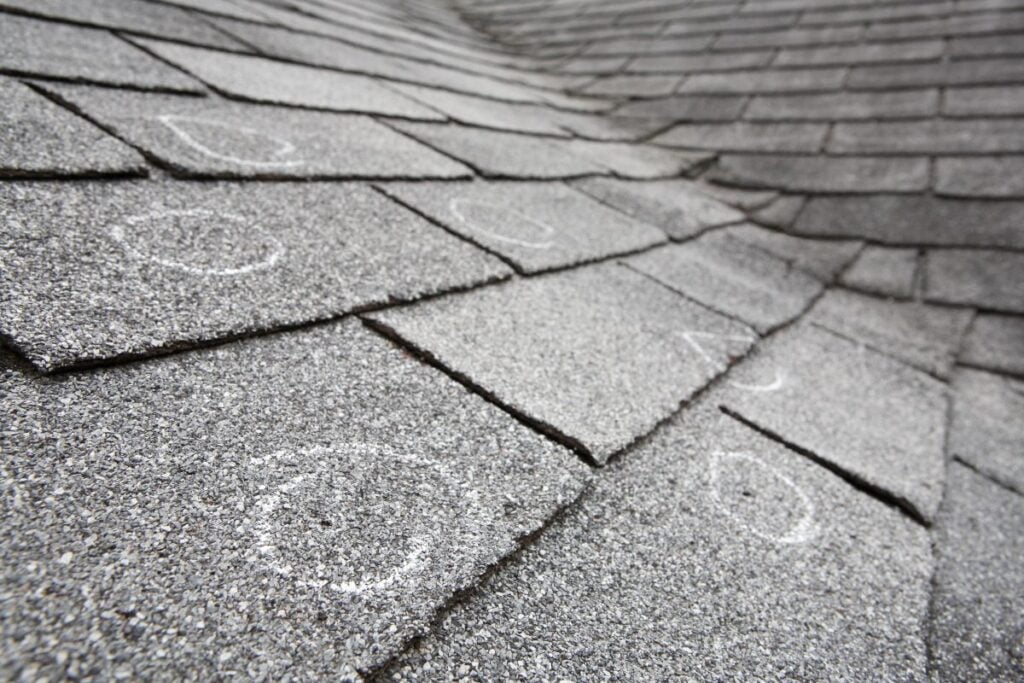 Close-up of gray asphalt roof shingles with several white chalk circles marking specific spots, indicating areas of possible damage or inspection points—important details to document when assessing the average insurance payout for hail damage roof claims.