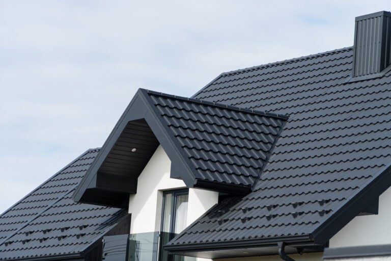 Black metal roofing tiles cover a modern house with a gabled design, set against a clear sky. The roof has clean lines and a contemporary look, hinting at durability and style.