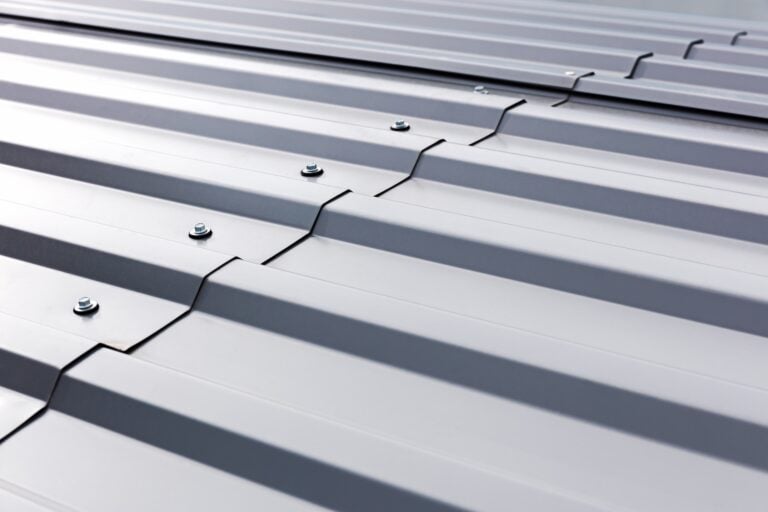 Close-up view of a gray metal roof with overlapping corrugated panels, visible screws, and ridges running horizontally across the surface—ideal for demonstrating how to seal corrugated metal roof seams effectively.