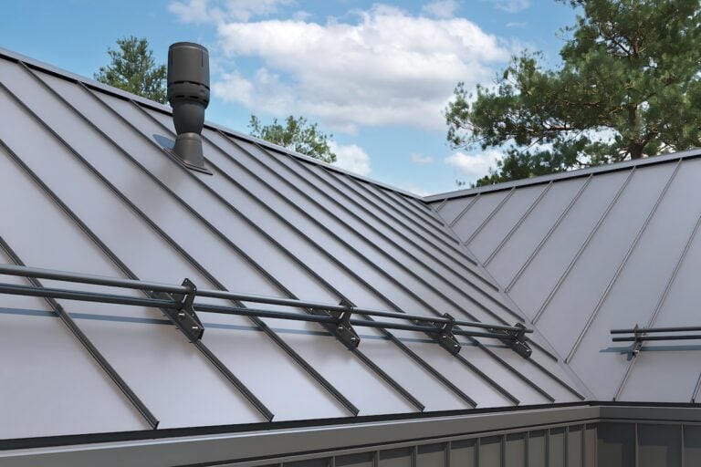 A standing seam metal roof, known for its durability and energy efficiency, features vertical seams and mounted snow guards under a partly cloudy sky, with trees in the background—an investment worth considering when factoring in standing seam metal roof cost.