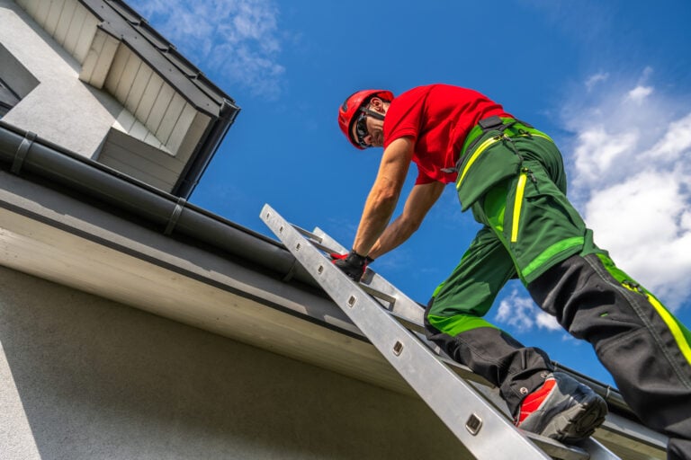 A worker wearing safety gear climbs a ladder to perform a roof inspection McLean on a modern house under a sunny sky, with scattered clouds in the background.