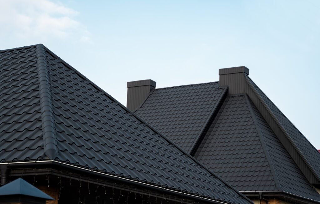 Roofing Trends McLean Steep, dark metal roofs with ridged panels and tall chimneys on two modern houses, set against a clear blue sky.