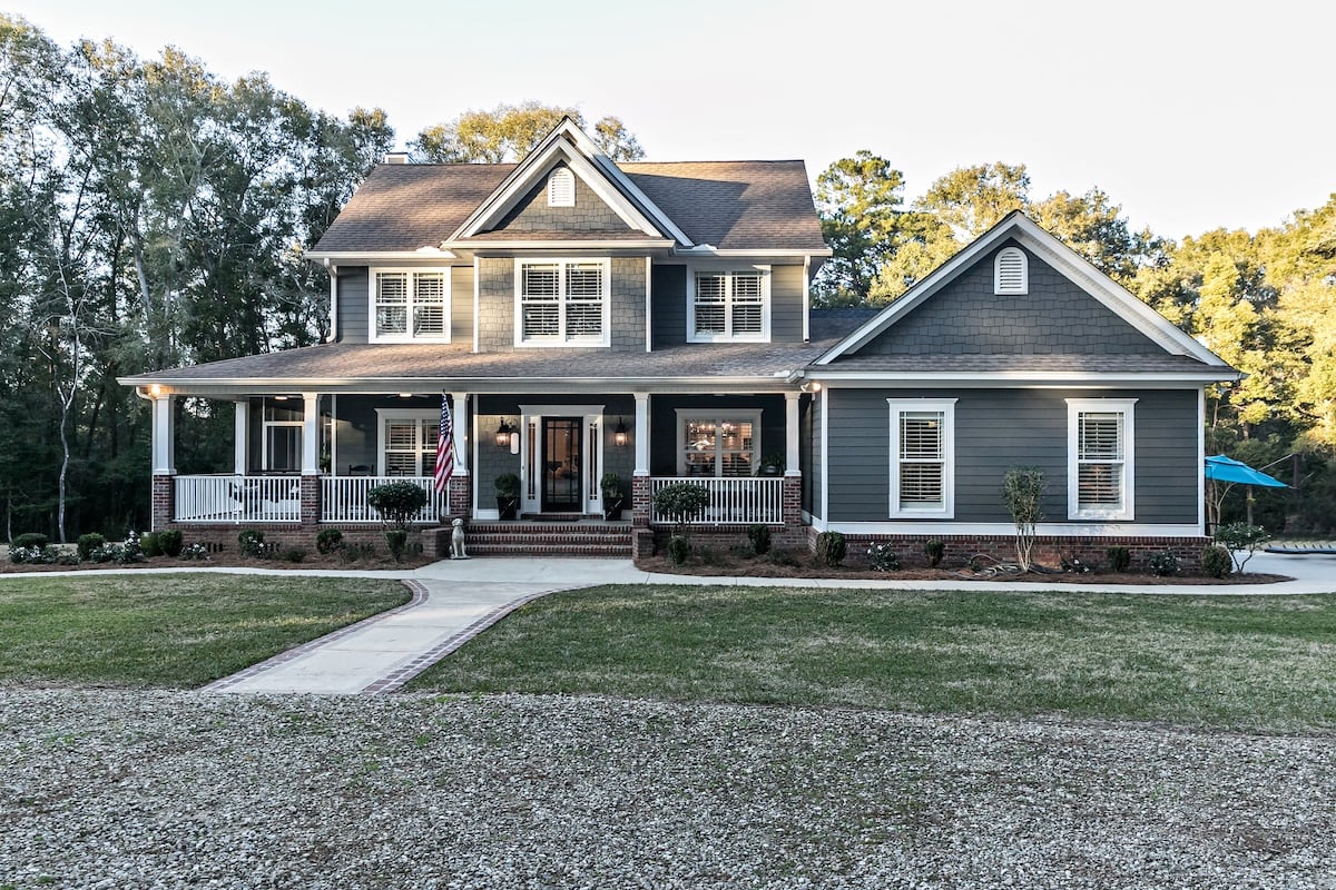 Roofing Warranties McLean Front view of a large two story blue gray house with wood and vinyl siding with an expansive porch, sidewalk and manicured lawn.