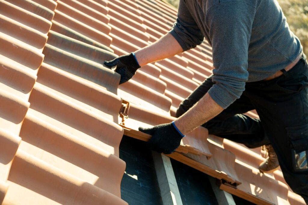 Closeup of worker hands installing yellow ceramic roofing tiles mounted on wooden boards covering residential building roof under construction