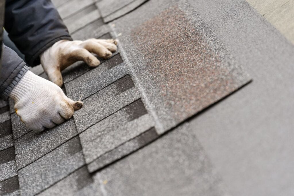 hand installing asphalt shingles on a roof