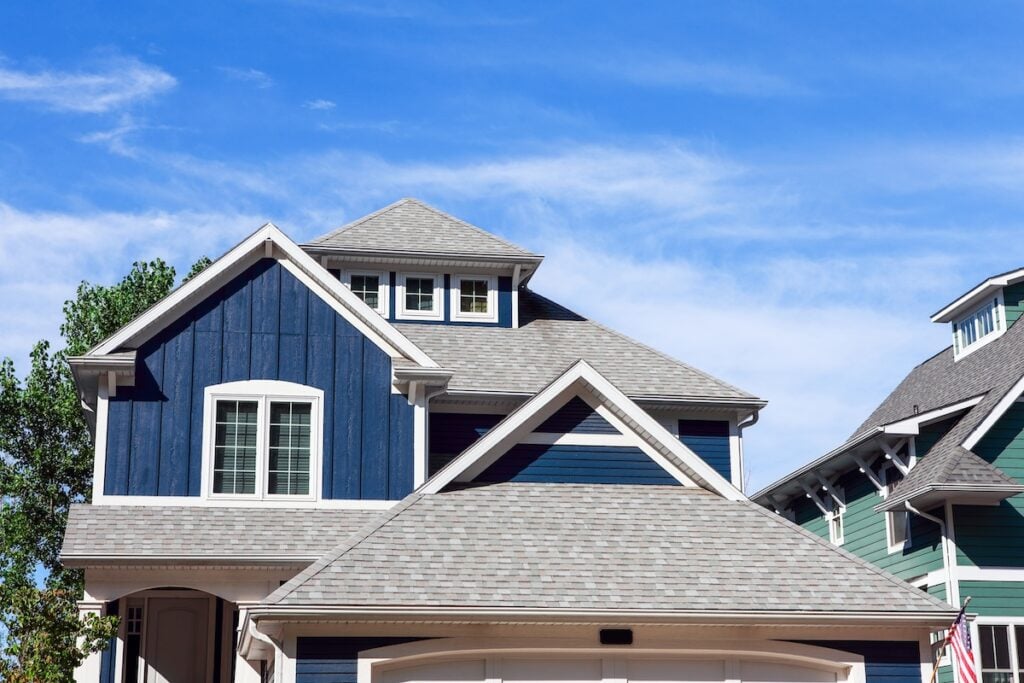 Two modern houses with gray shingle roofs and blue siding under a clear blue sky. The house in the foreground, expertly crafted by roofing Burke specialists, is navy blue with white trim around the windows and roof.