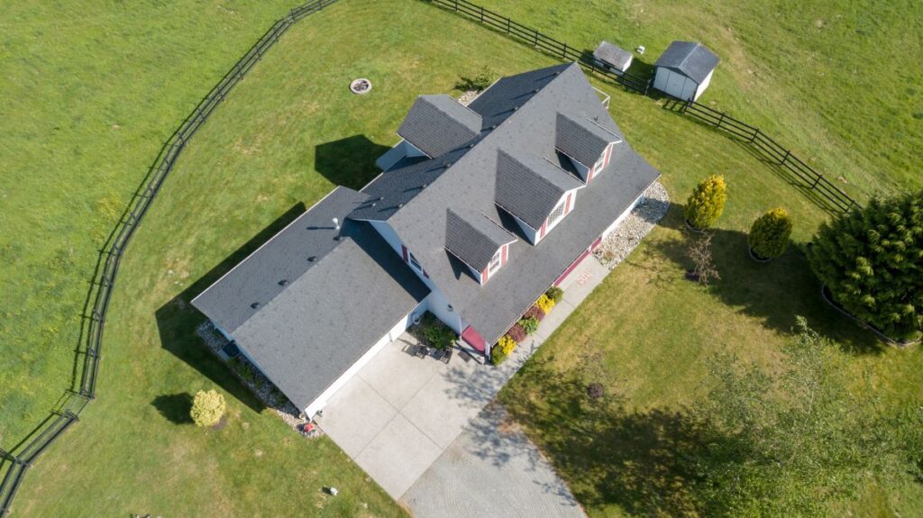 Aerial view of a house with a gray roof, white exterior, and red accents, located in Springfield. Surrounded by a green lawn, black fence, small shed, trees, and a concrete driveway—showcasing expert roofing Springfield homeowners trust.