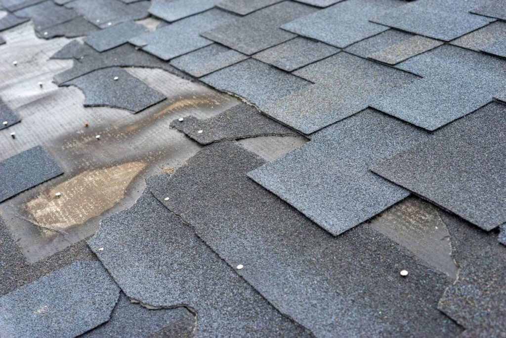 Close-up of a damaged asphalt shingle roof in Springfield with missing, misaligned, and lifted shingles exposing underlying roofing material and nails, indicating wear and potential water damage—ideal for roofing Springfield repairs.