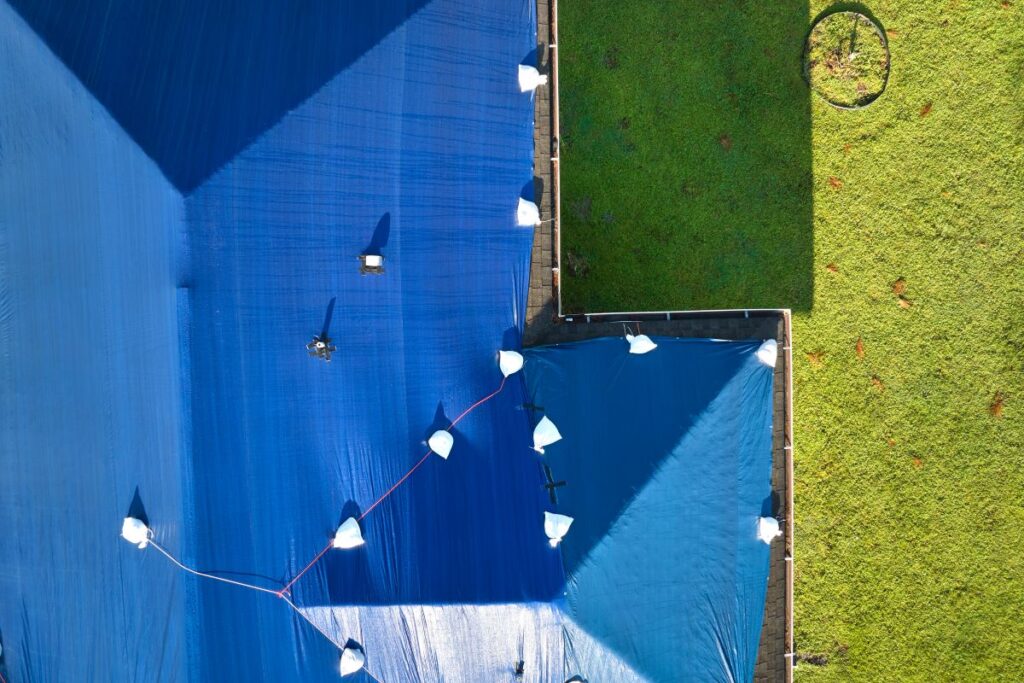 Aerial view of a building in Springfield covered with large blue tarps, secured by white sandbags. Part of a green grassy yard appears on the right, while a person walks across the tarp—showcasing roofing springfield repairs in progress.