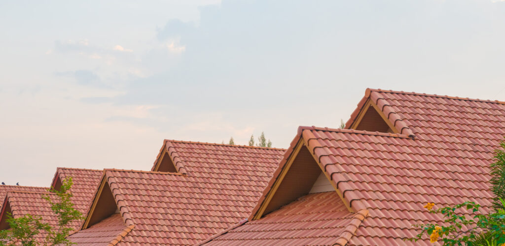 A row of houses with red tiled roofs and gable ends, set against a cloudy sky with some trees partially visible in the foreground—showcasing quality roofing McLean VA residents appreciate.