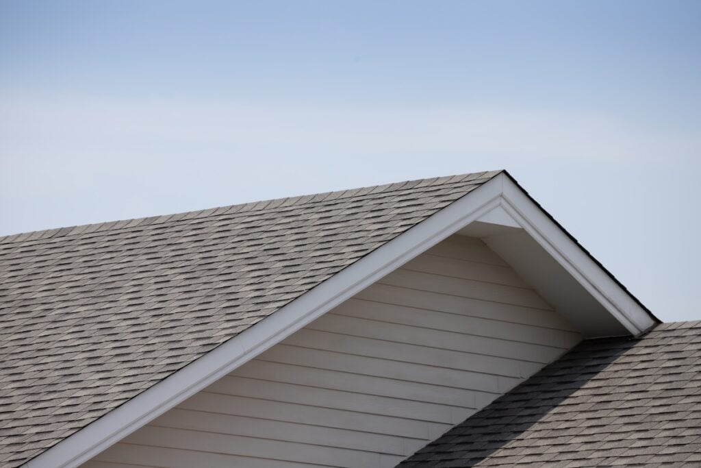 Close-up of a house roof with gray asphalt shingles and white trim, triangular gable, and clear blue sky—showcasing expert roofing Arlington VA craftsmanship.