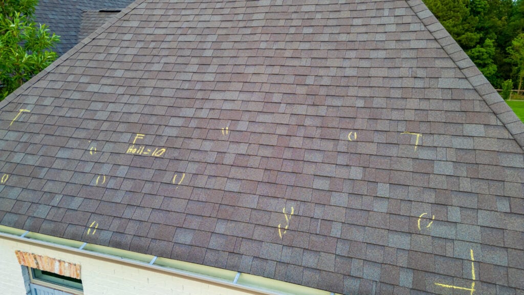 A house roof with brown shingles marked with yellow chalk lines and symbols, possibly for inspection or repair. Trees and grass are visible in the background, reflecting typical roofing McLean VA projects.