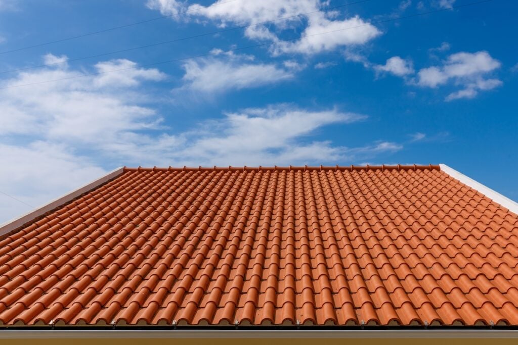A house roof covered with orange terracotta tiles, a popular choice among roof materials in Falls Church, is shown against a blue sky with scattered white clouds.