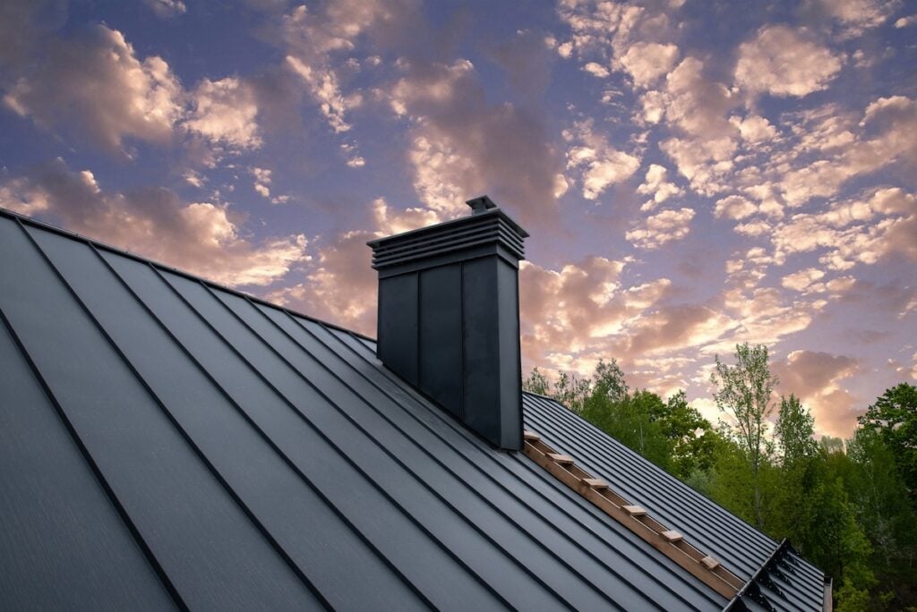 roof materials springfield A modern metal roof with a black chimney rises against a dramatic sky filled with scattered clouds at sunset. Trees with green foliage are visible in the background.