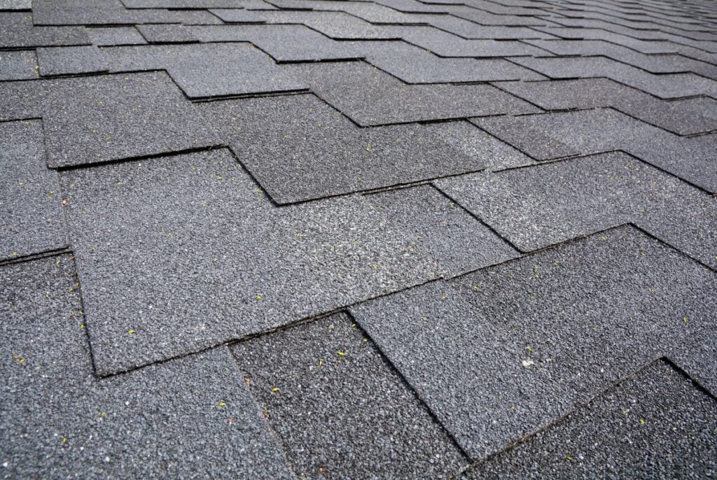 Close-up view of overlapping gray asphalt roof shingles arranged in a neat, staggered pattern, showing the texture and detail of the roofing material.