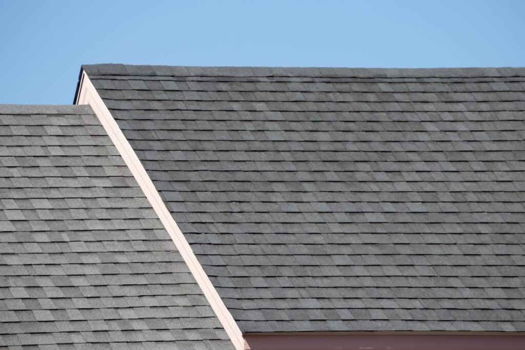 Gray shingle rooftops of two adjacent houses with a clear blue sky in the background. The roofs create geometric angles and lines across the image.