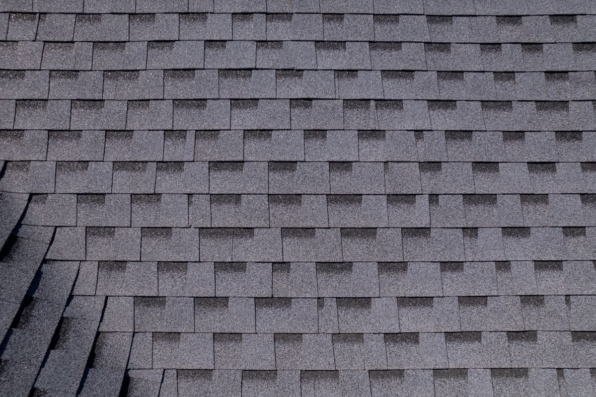 Close-up view of overlapping gray asphalt roof shingles arranged in a neat, repetitive pattern, with a small section on the lower left appearing slightly uneven.