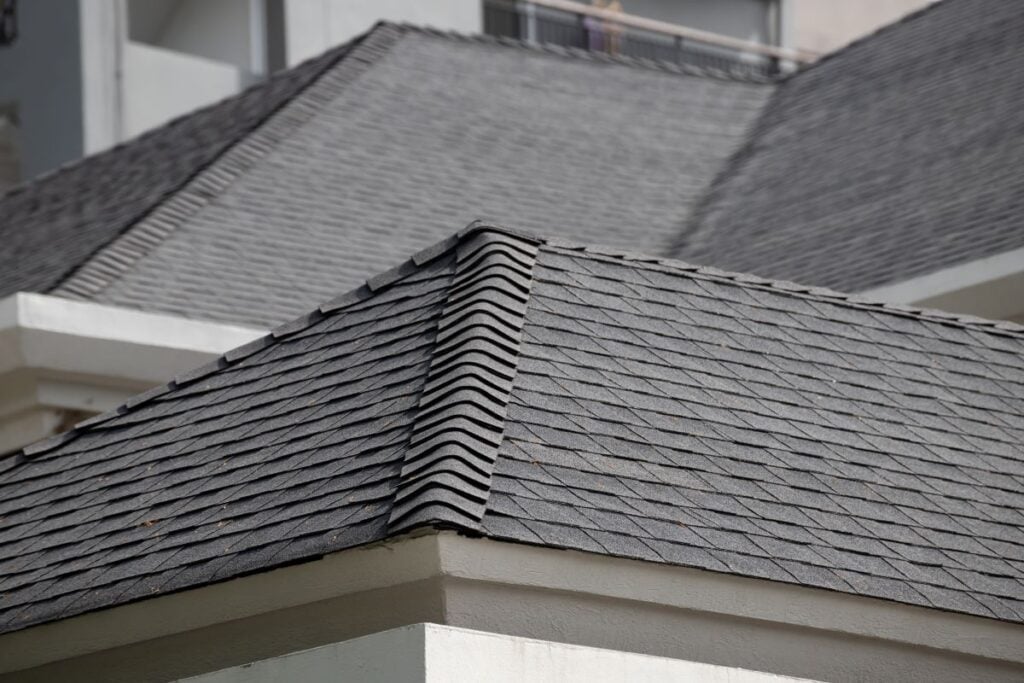 Close-up view of intersecting rooftops covered with dark gray asphalt shingles on a light-colored building, showing detailed texture and neat alignment of the roofing materials.