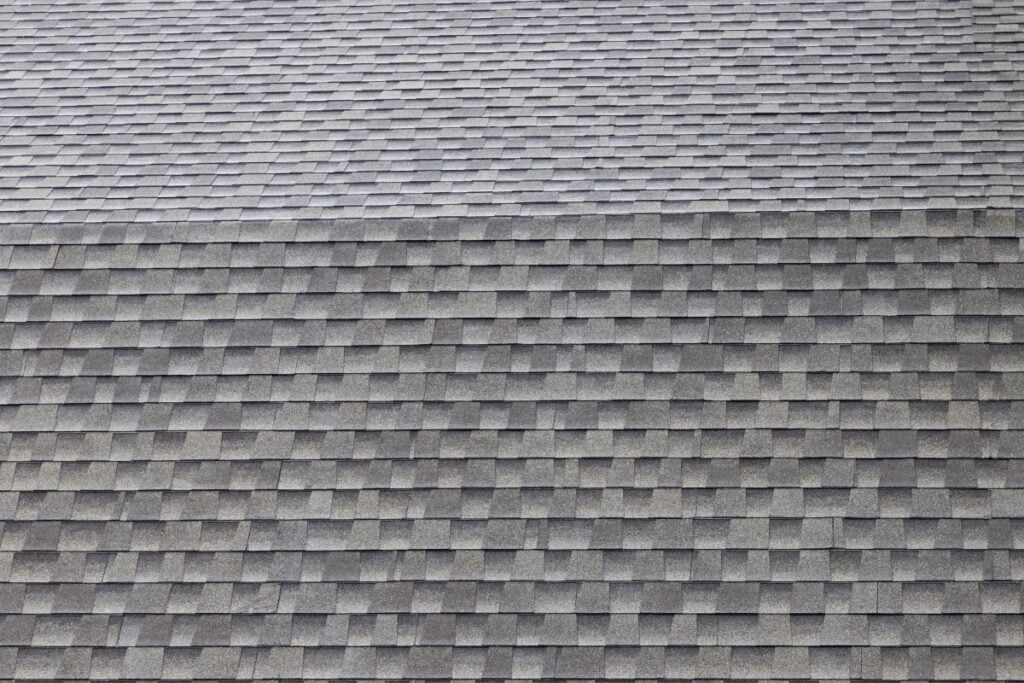 Close-up view of a roof covered with overlapping gray asphalt shingles arranged in a uniform, repetitive pattern.