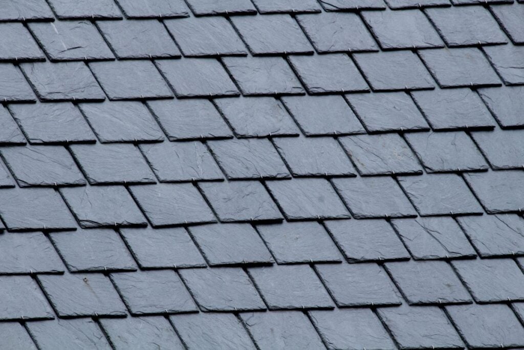 Close-up of overlapping rectangular gray roof shingles arranged in a diagonal pattern, creating a textured surface.