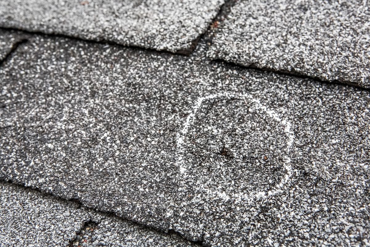 A close-up of asphalt roof shingles with a white chalk circle marking a damaged or worn spot on one shingle.