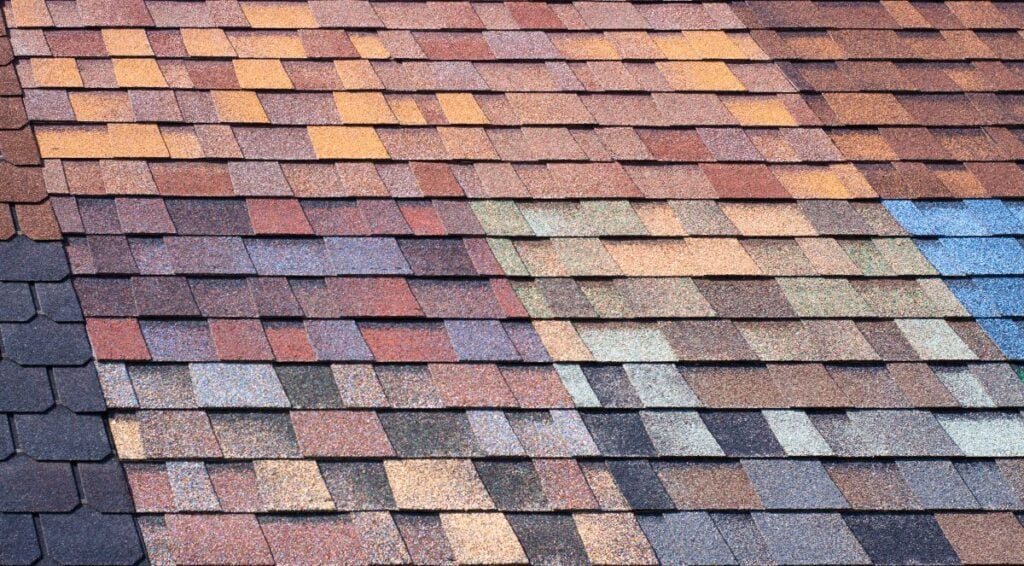 Close-up of a roof with multicolored asphalt shingles arranged in a regular overlapping pattern, displaying various shades of brown, orange, blue, and gray.