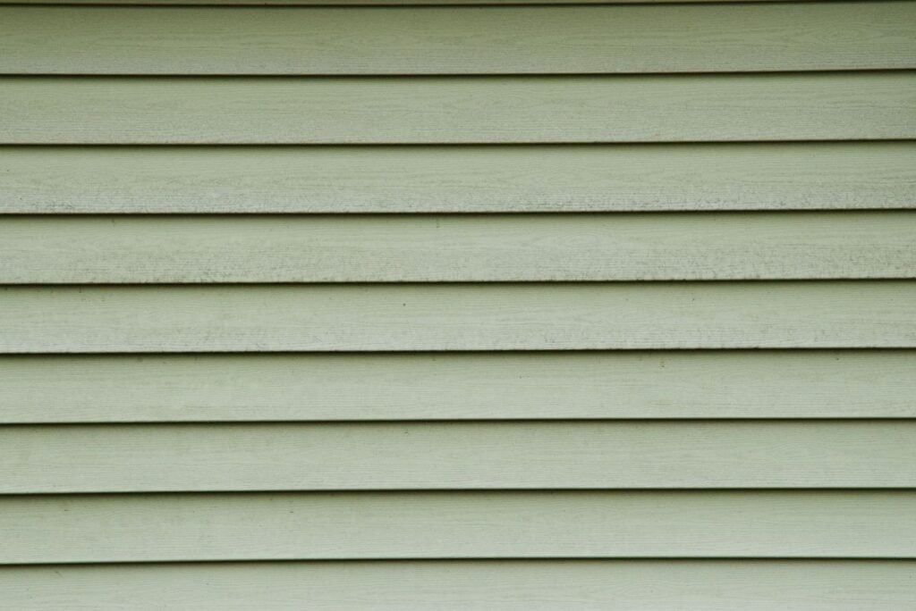 Close-up of pale green horizontal siding panels on a building exterior, showing slight weathering and texture.