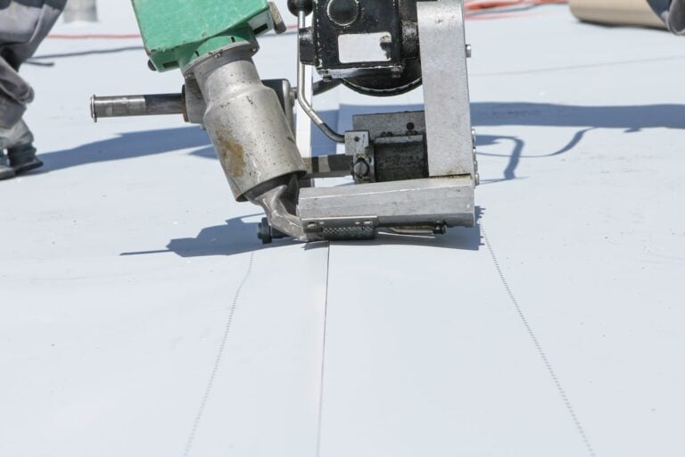 Close-up of a machine welding or sealing seams on a light-colored flat roof membrane, used in roofing construction.