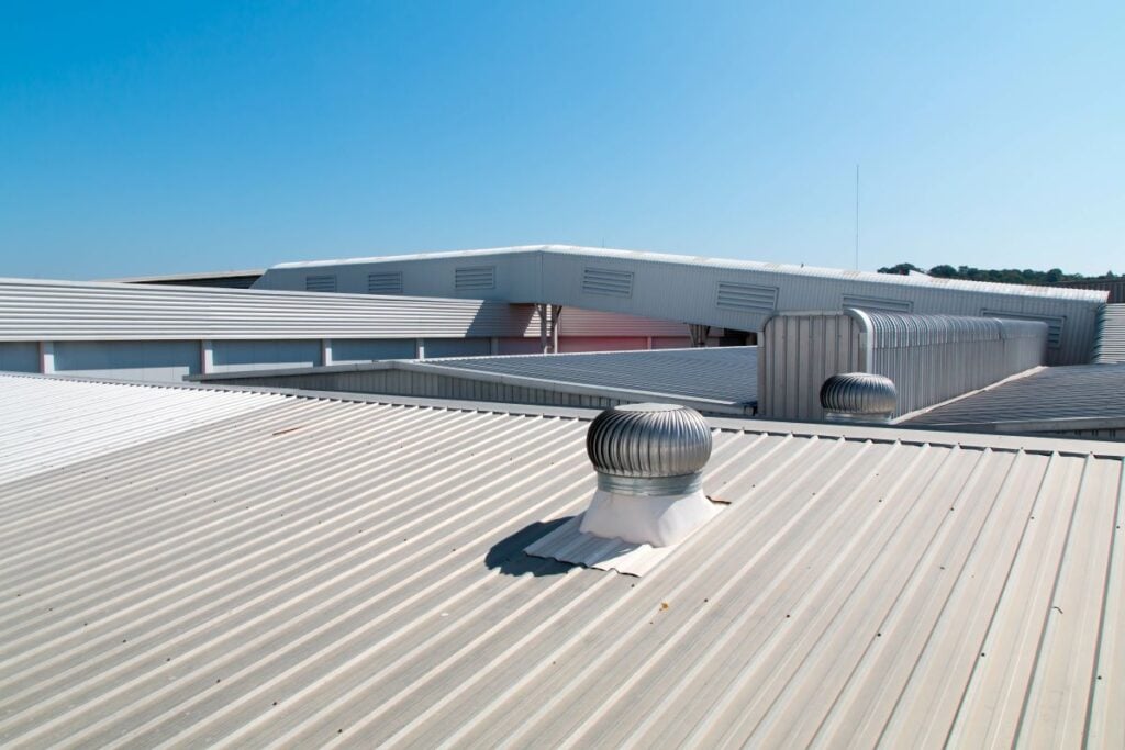 Two metal roof turbine ventilators on a corrugated metal factory roof under a clear blue sky.
