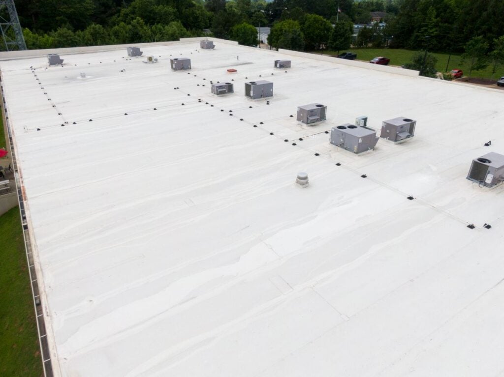 High-angle view of a flat, white commercial building roof with several HVAC units arranged in rows.