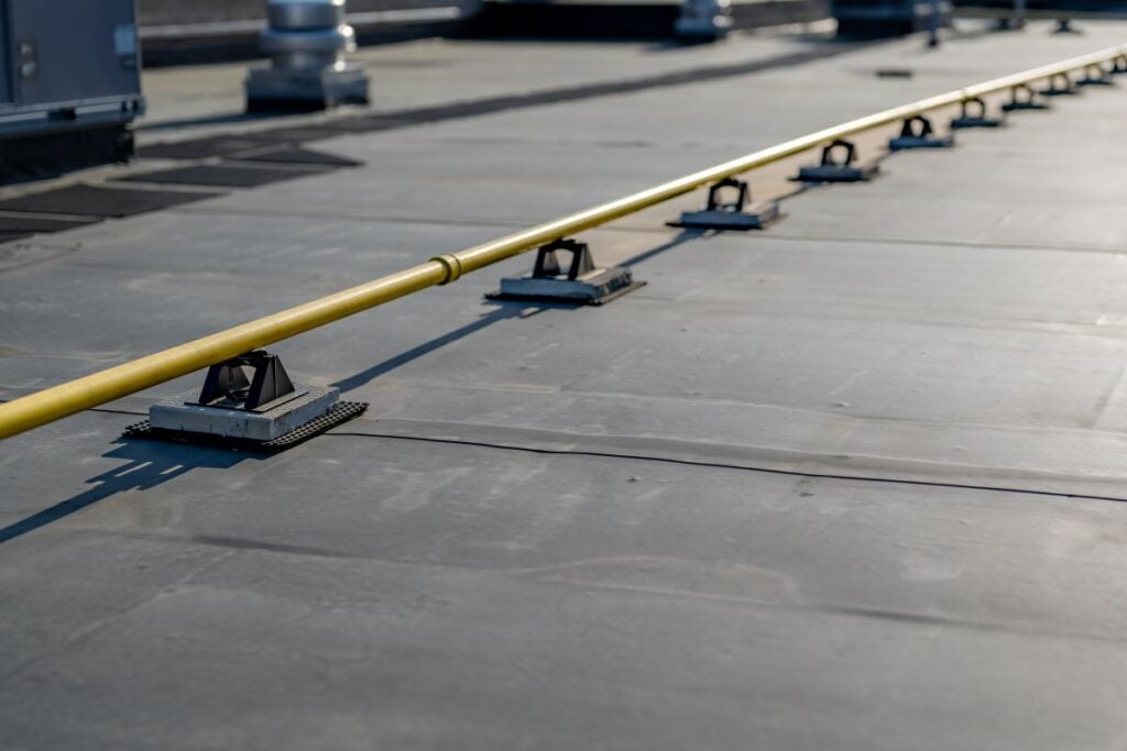 A yellow industrial pipe supported by brackets along a flat, gray rooftop.