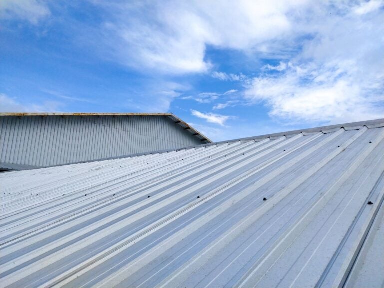 Corrugated metal roof against a bright blue sky with scattered clouds.