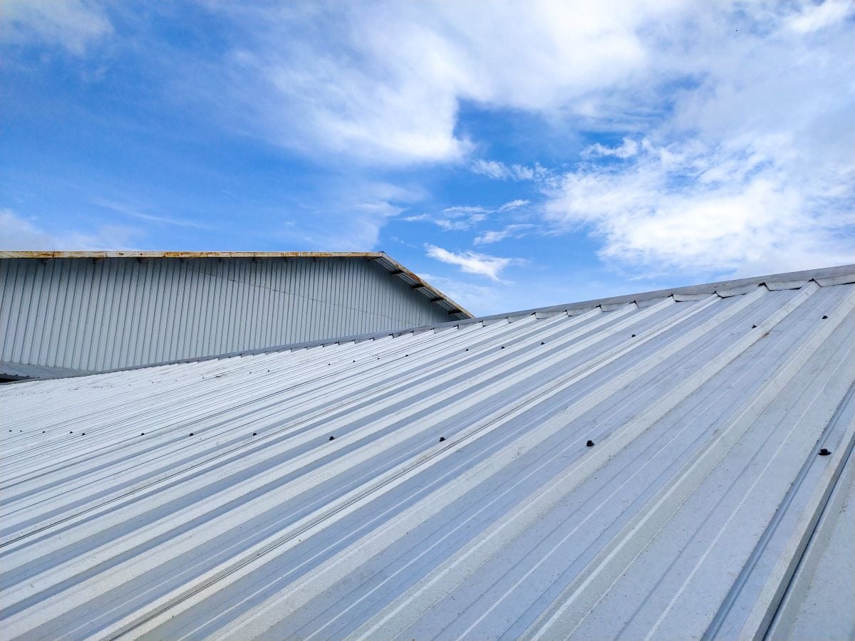 Corrugated metal roof against a bright blue sky with scattered clouds.