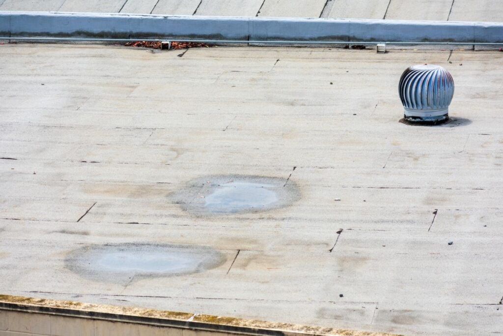A flat commercial roof with two shallow puddles and a single spinning metal roof vent.