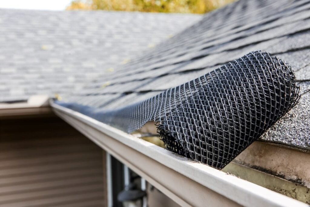 Black mesh gutter guard being installed along the edge of a shingled roof.