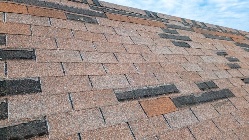 A sloped roof with missing and damaged asphalt shingles.