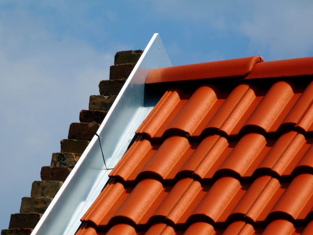 Red roof tiles meeting a brick chimney with a metal flashing strip.