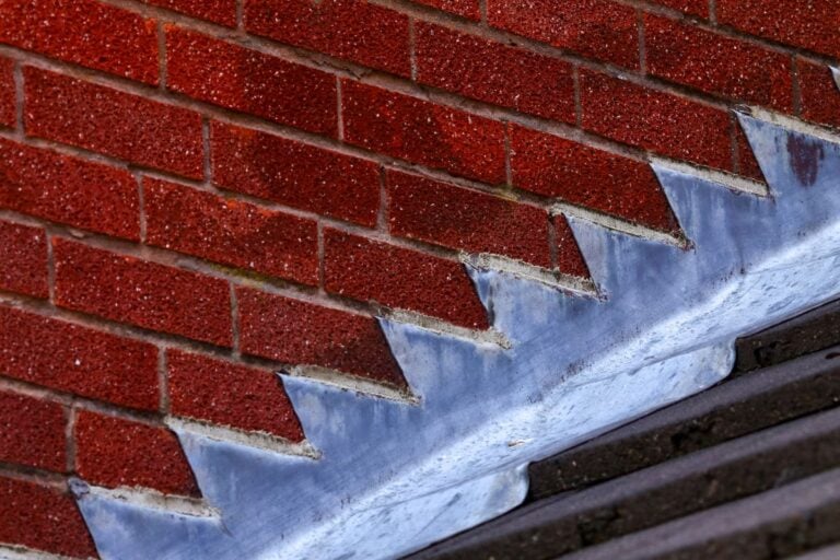 A jagged, saw-toothed metal flashing strip set against a red brick wall above a roofline.