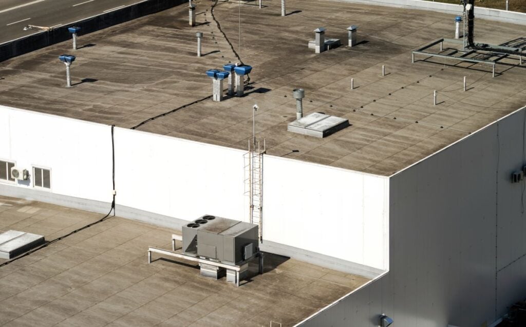 High-angle view of a large commercial building roof with various HVAC units, exhaust vents, and a vertical ladder.