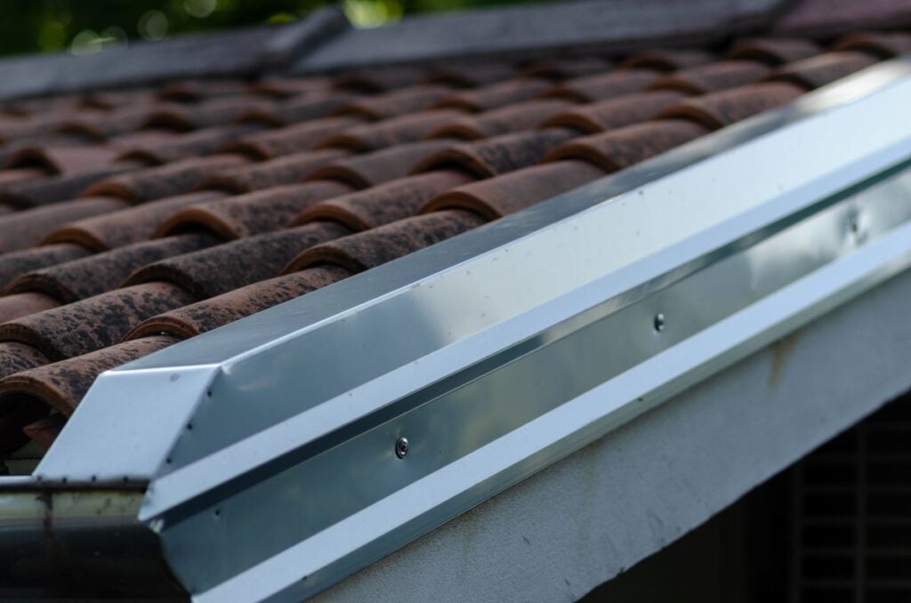 A close-up of a metal roof gutter installed along the edge of a clay tile roof.