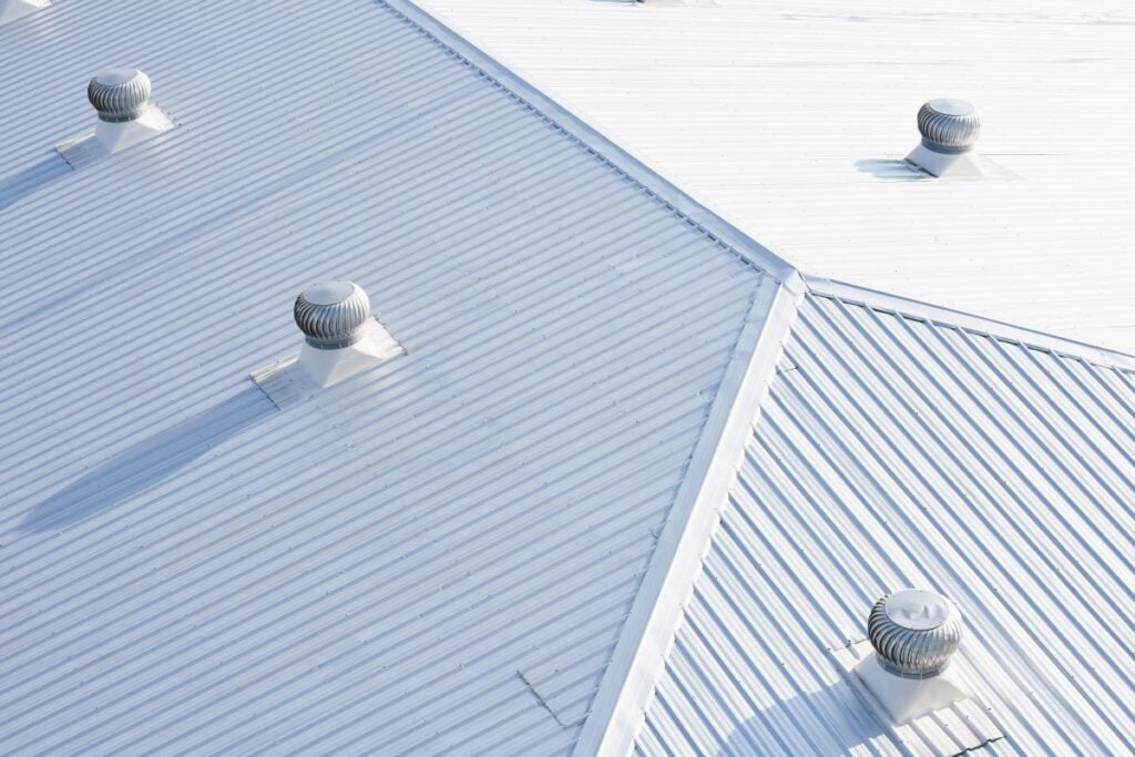 Four wind-driven roof turbine ventilators on a white corrugated metal roof.