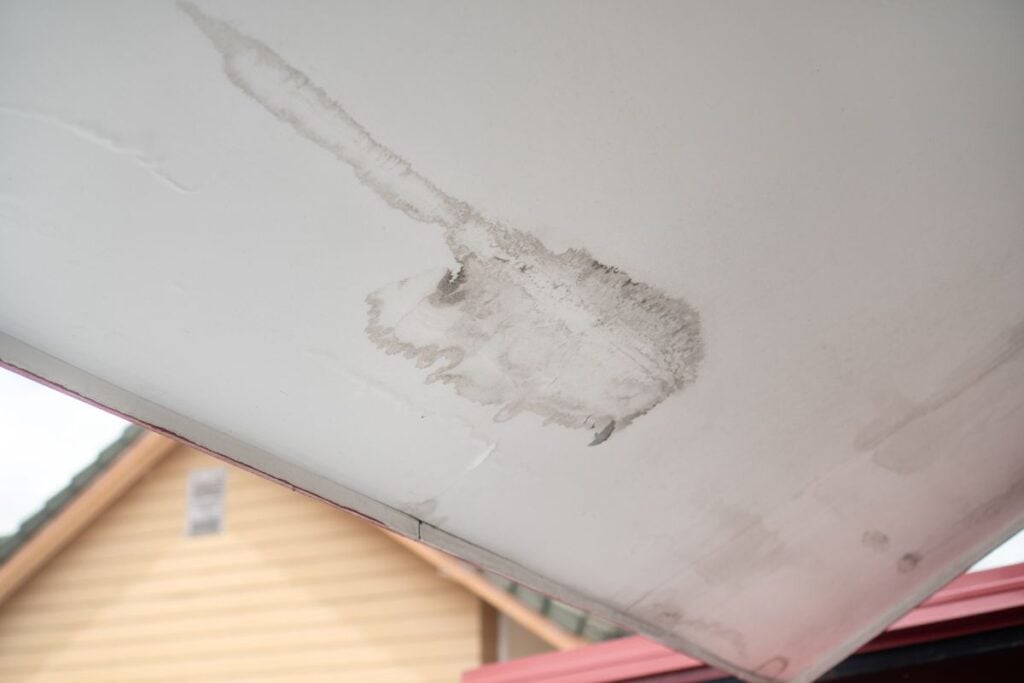A large water stain and peeling paint on a white ceiling.