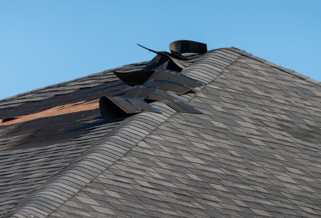 Damaged asphalt roof shingles curling and lifting along the ridge line of a house.